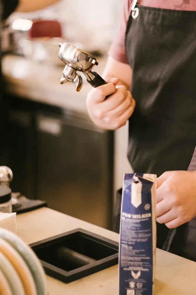 Barista holding a portafilter preparing coffee in a cozy café environment.