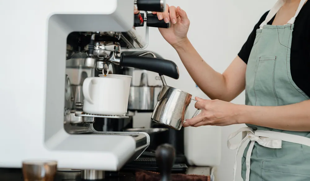 A barista prepares a coffee using an espresso machine in a modern café.