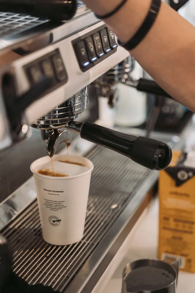A barista brews fresh coffee into a paper cup using an espresso machine.