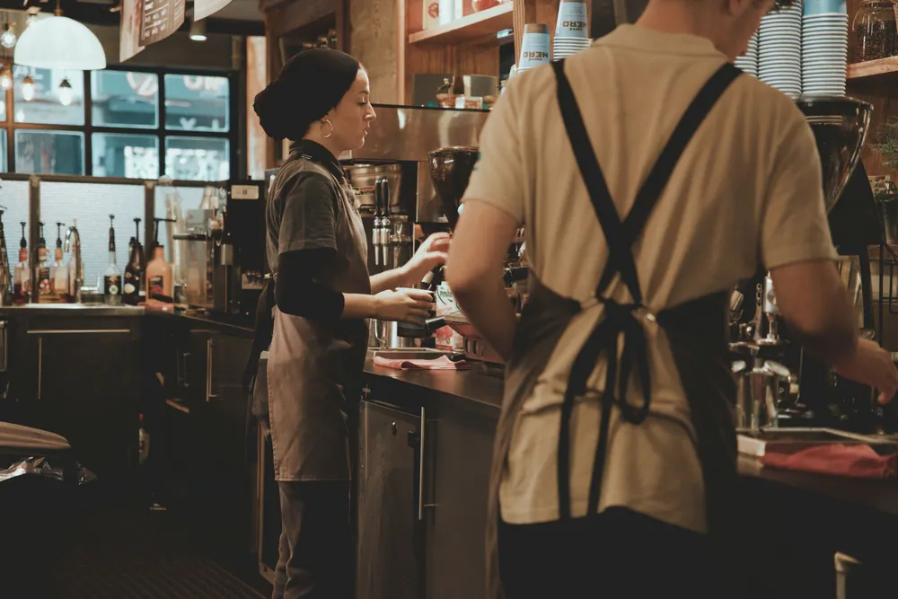 Baristas at work in a cozy café, using coffee machines to prepare drinks.