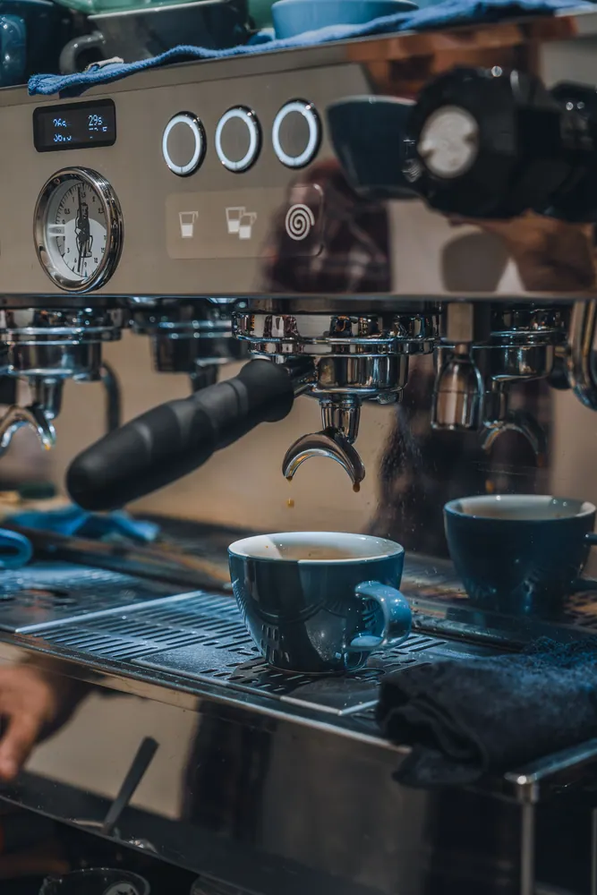A professional espresso coffee machine making coffee with a blue cup in a cafe setting.