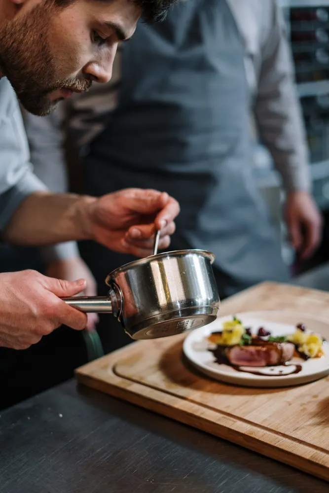 Chef adding final touches with sauce to a gourmet dish in a professional kitchen setting.