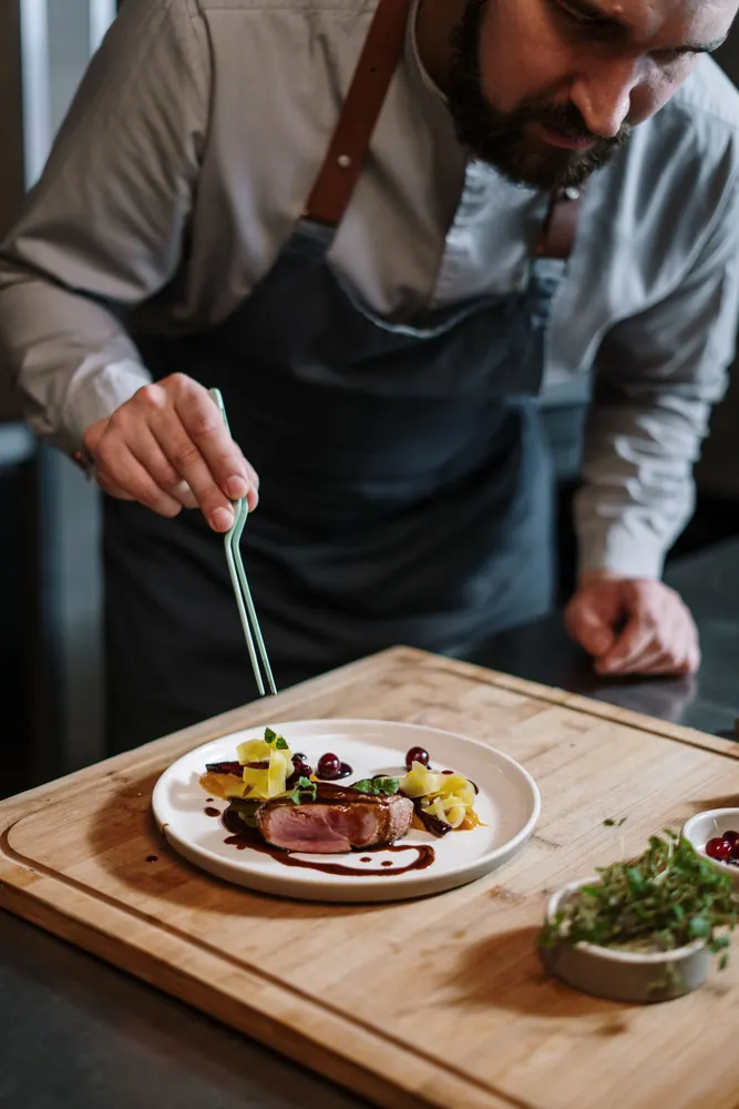Chef artistically plating a gourmet dish with precision in a modern kitchen setting.