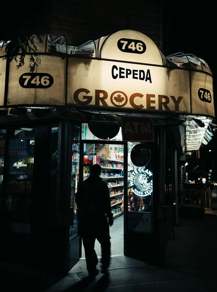 Silhouette of a person entering Cepeda Grocery under neon lights, New York City at night.