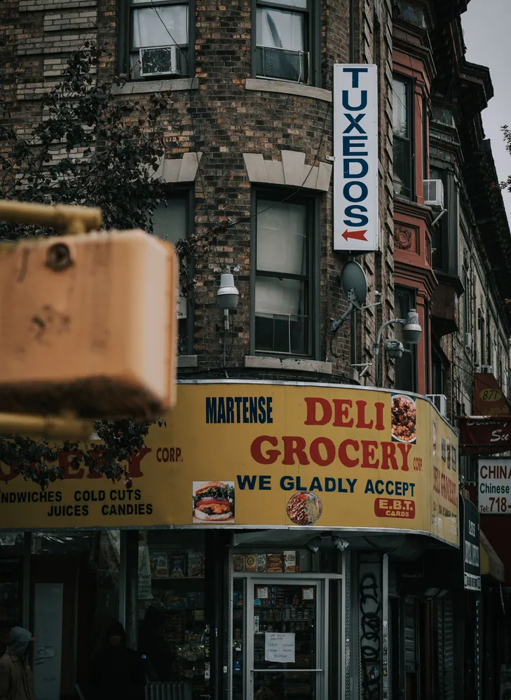 Classic New York street featuring a deli grocery and tuxedo shop sign, capturing urban life.