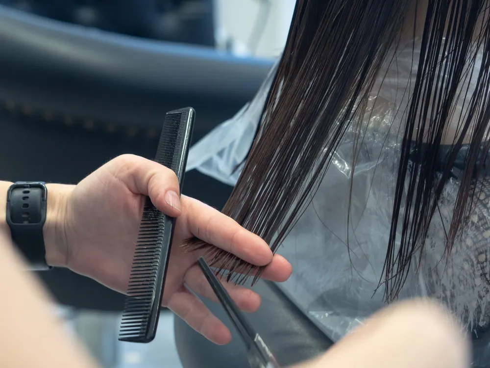 Close-up of a professional haircut in progress at a salon, highlighting comb and scissors.