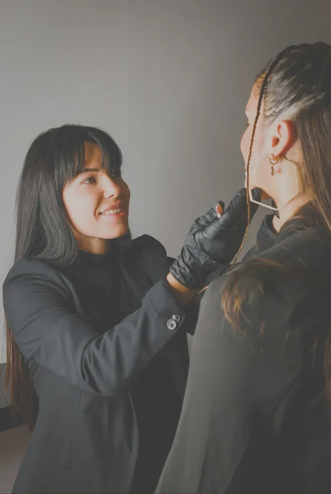 A stylist adjusts a client's hair in an indoor setting, showcasing fashion and beauty expertise.