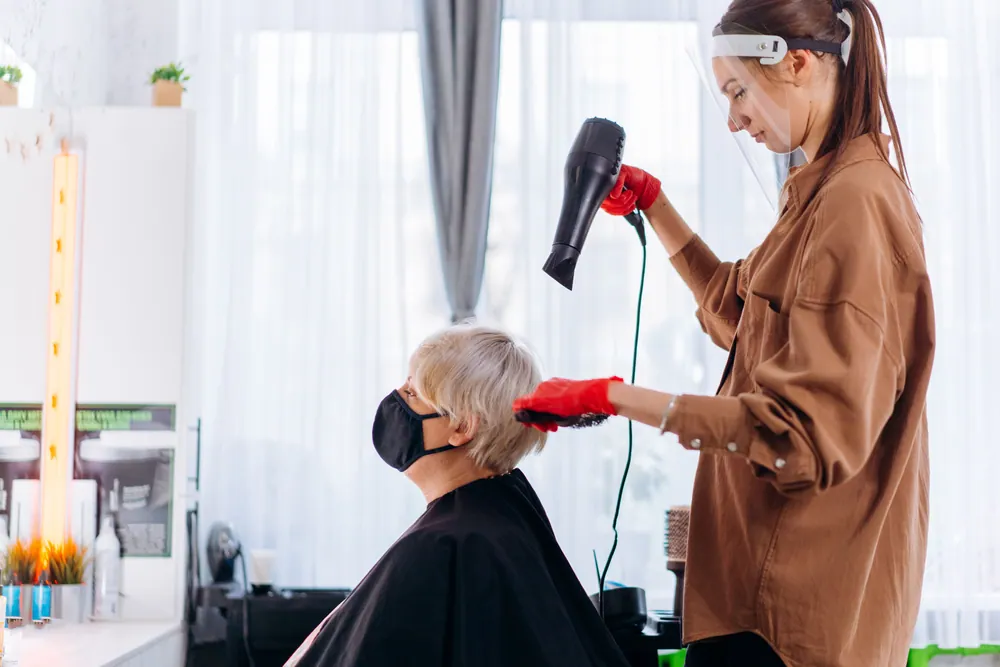 Senior woman gets a stylish haircut indoors by a professional hairstylist wearing protective gear.