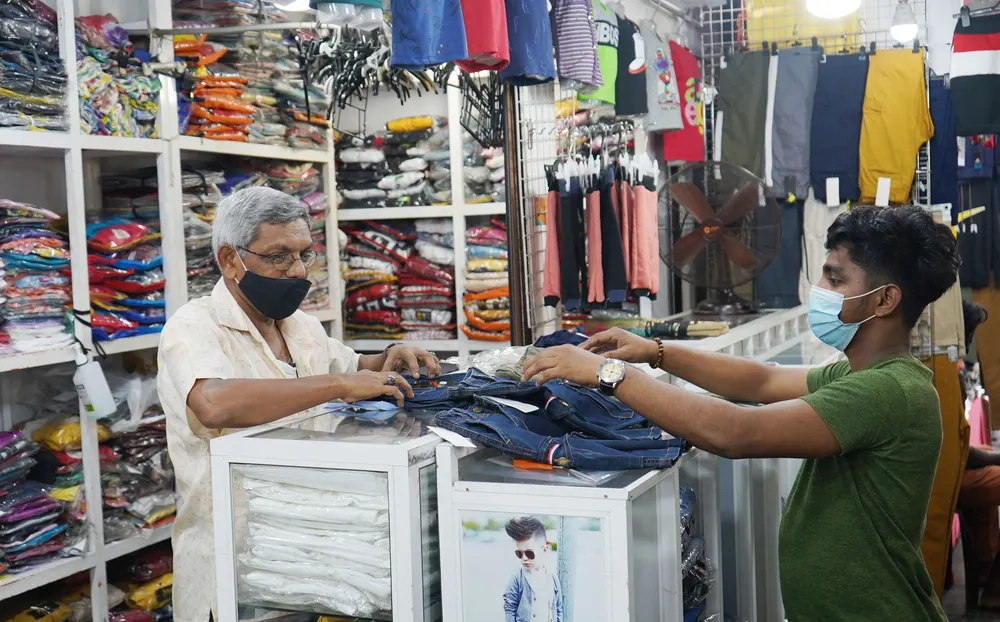 Two men in masks engage in a clothing purchase in an indoor store setting.