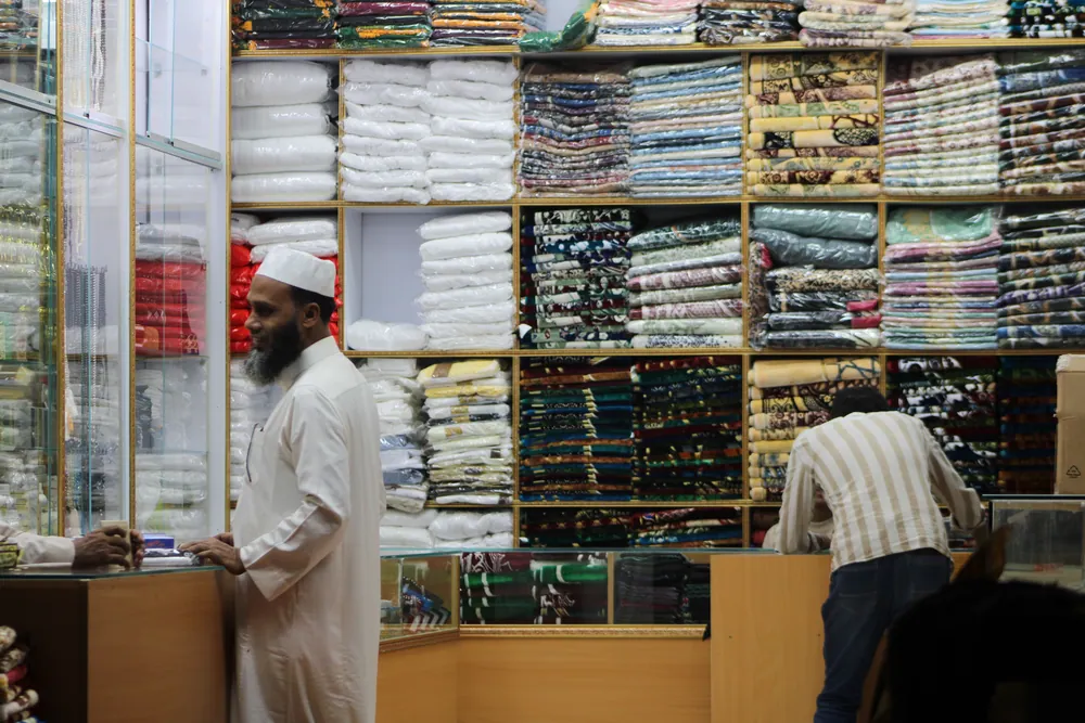 Two men interacting in a colorful fabric store filled with various textiles and cloth materials.