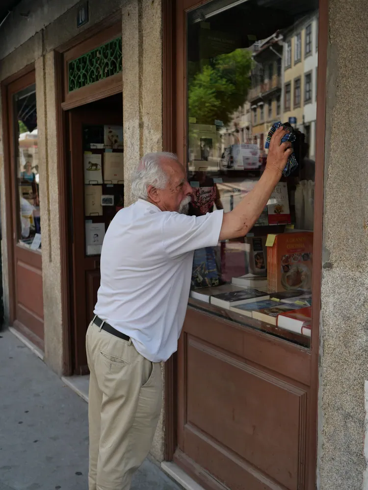 Senior man cleaning shop exterior window on a city street, focused and diligent.