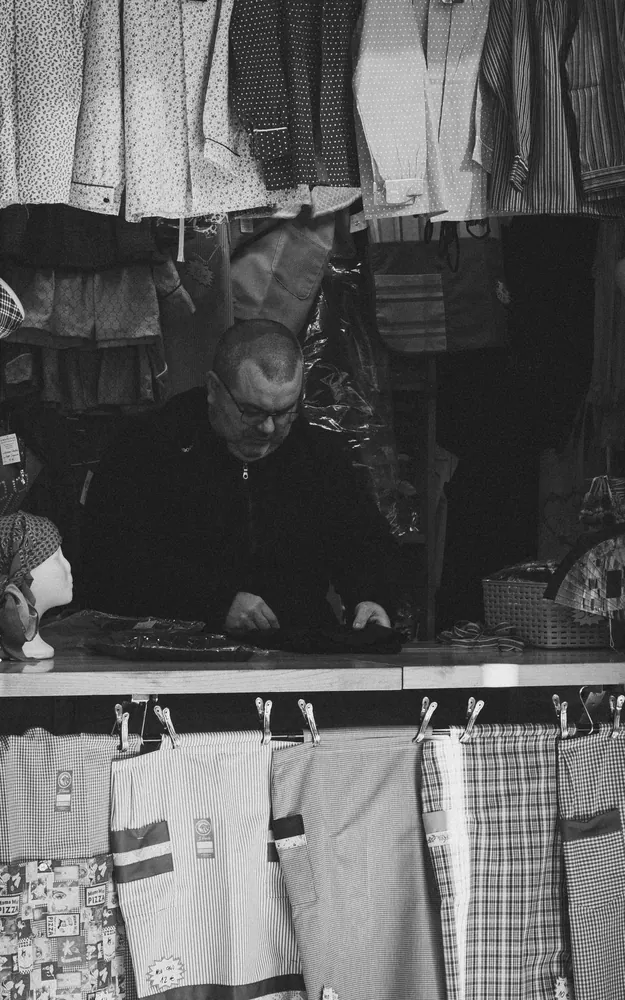 Black and white photo of a man selling fabrics at a market stall in Valencia, Spain.