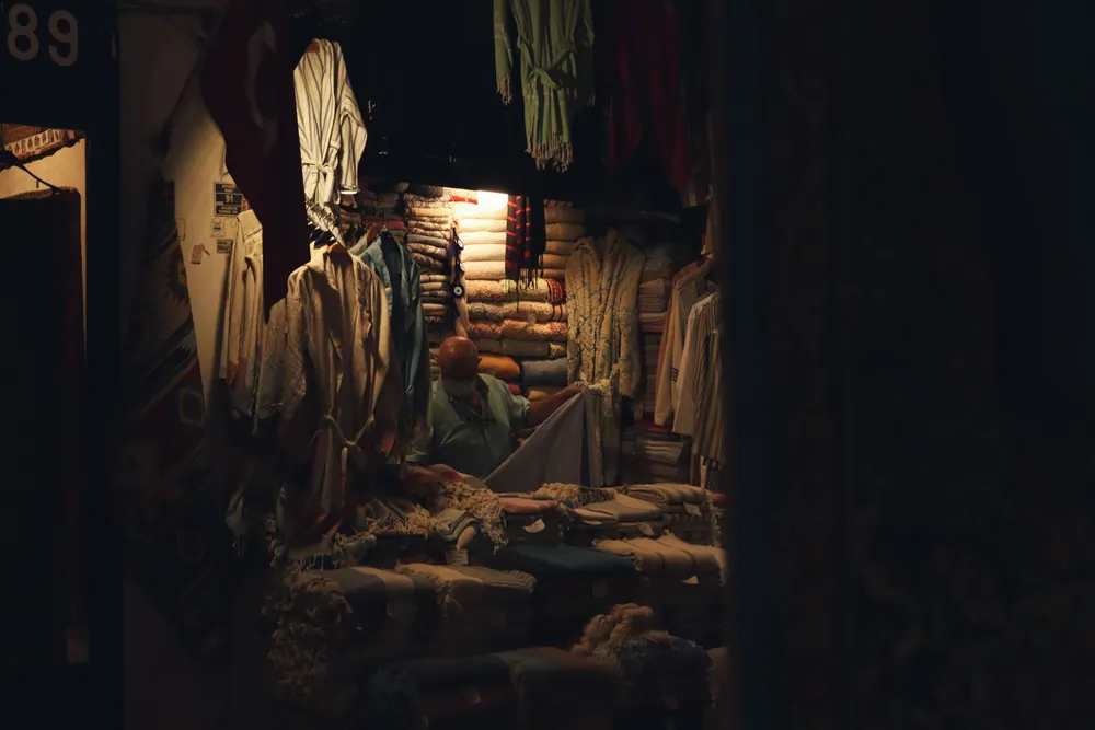 A cozy textile shop with stacks of colorful fabrics and clothes in dim lighting.