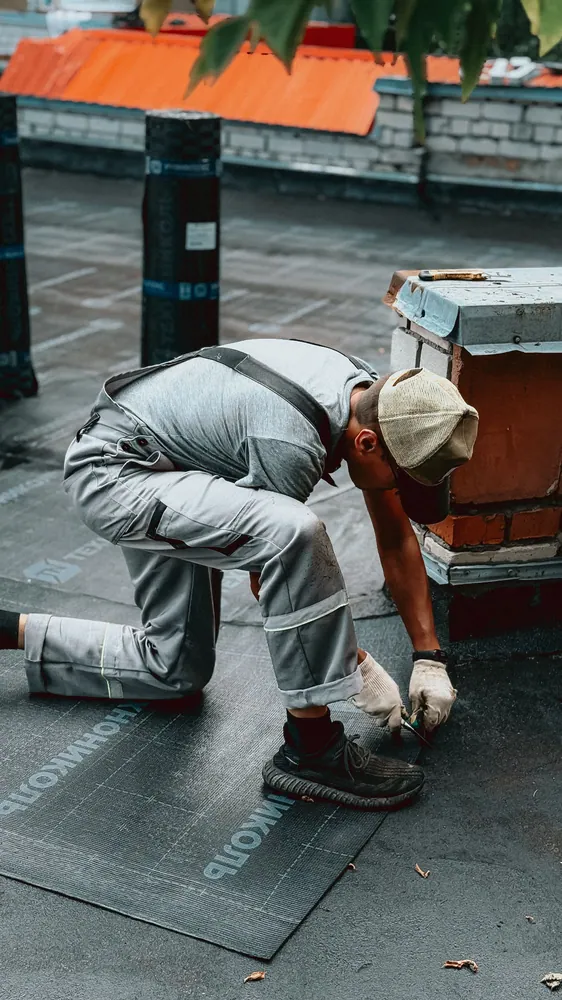 A roofer in protective clothing repairing an urban rooftop on a sunny day.