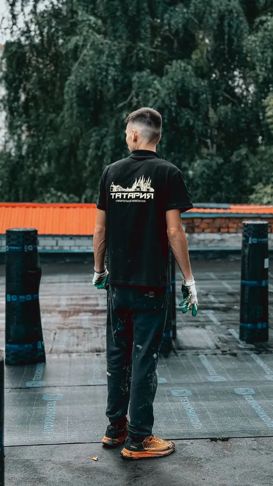 A person working on a rooftop with trees in the background on a cloudy day.