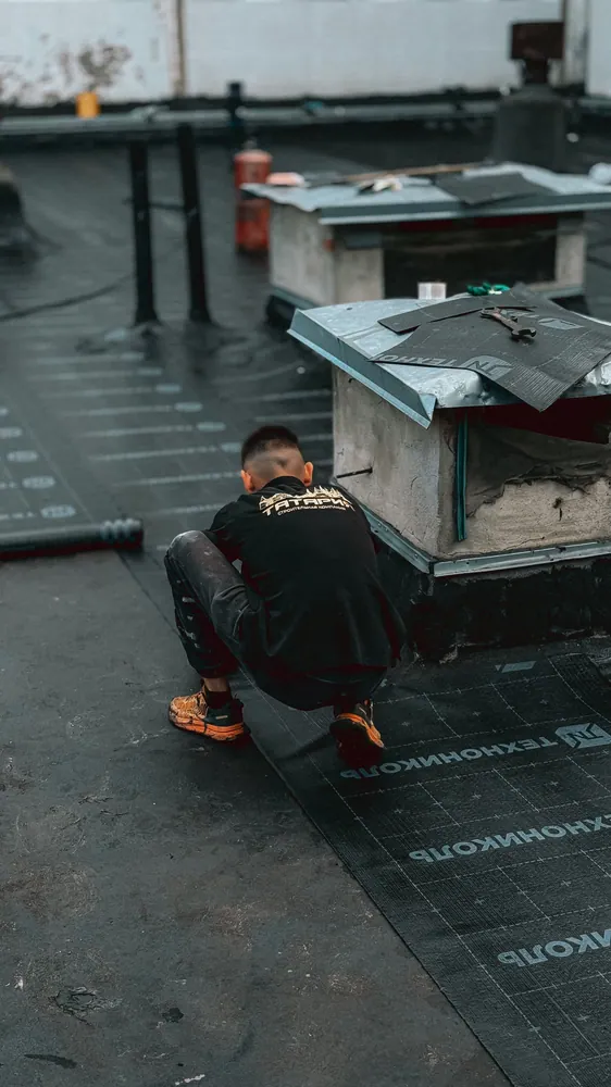 Man crouched on rooftop installing waterproof membrane, focused on repair work