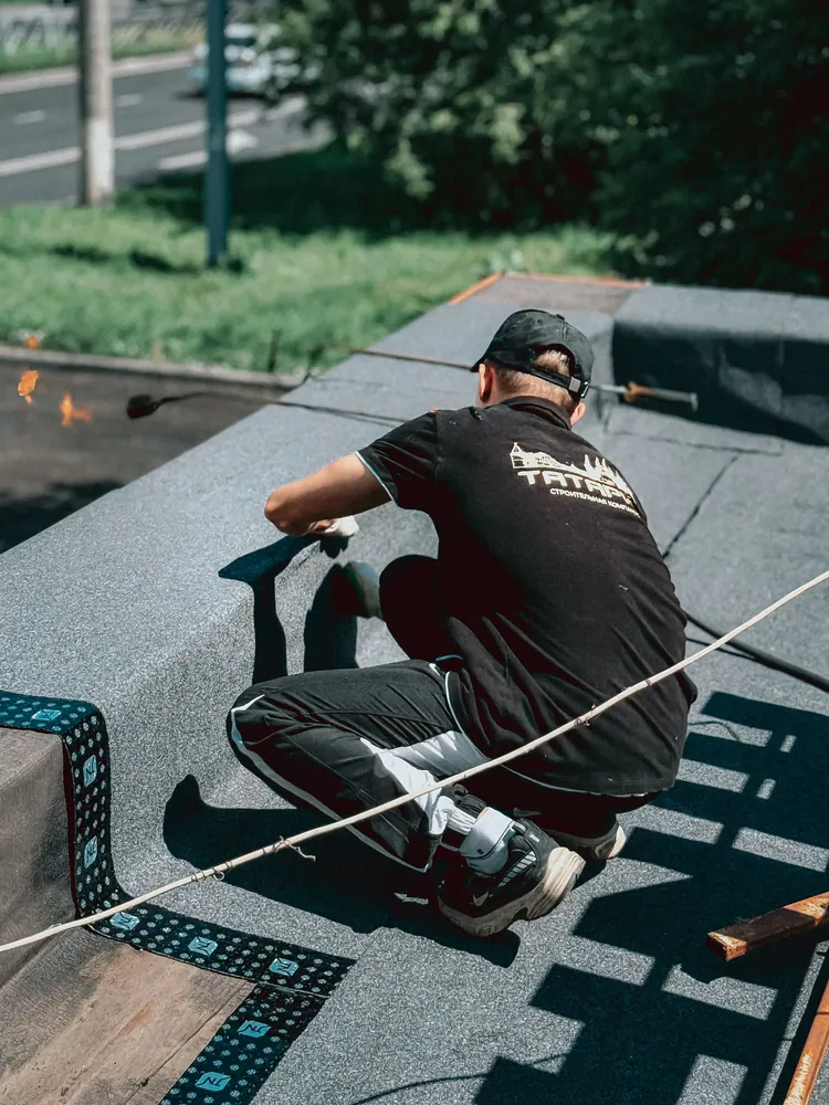 A roofer installs roofing material on a flat roof under sunny conditions, showcasing precise craftsmanship.