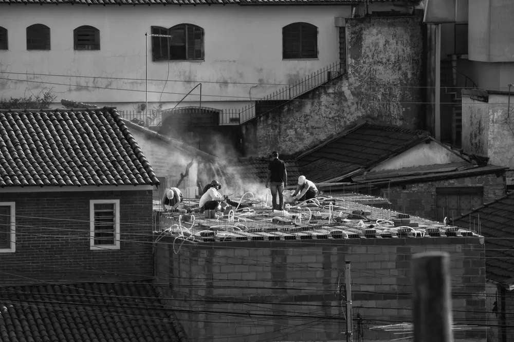 Black and white image of workers on a rooftop in an urban setting, suggesting construction work.