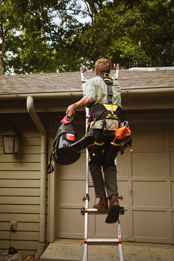 A construction worker in safety gear climbs a ladder for roof work in North Carolina.